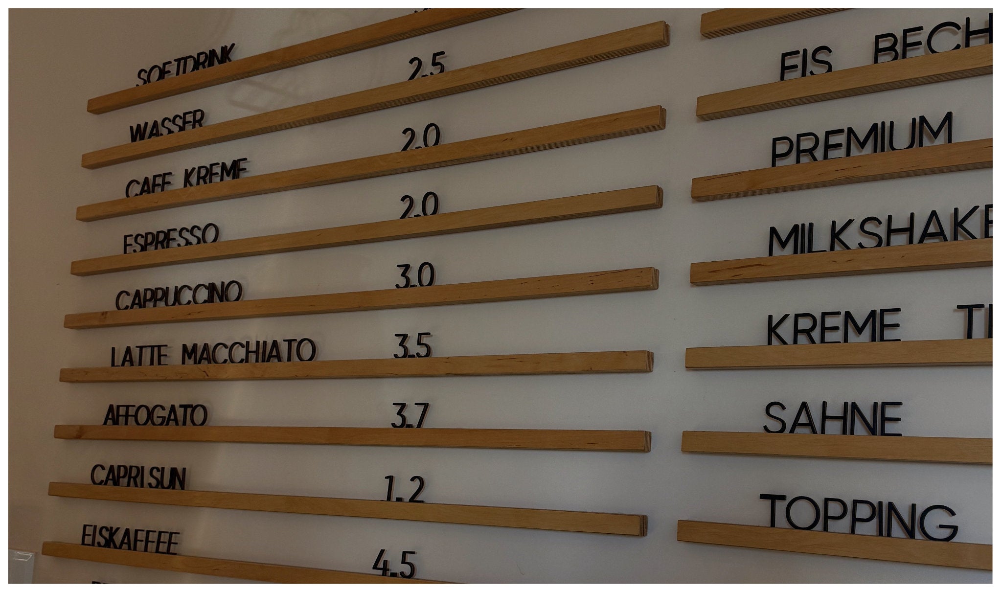 Minimalistische Café-Preistafel mit Holzleisten und schwarzen Buchstaben – Preise für Getränke wie Espresso, Cappuccino und Softdrinks