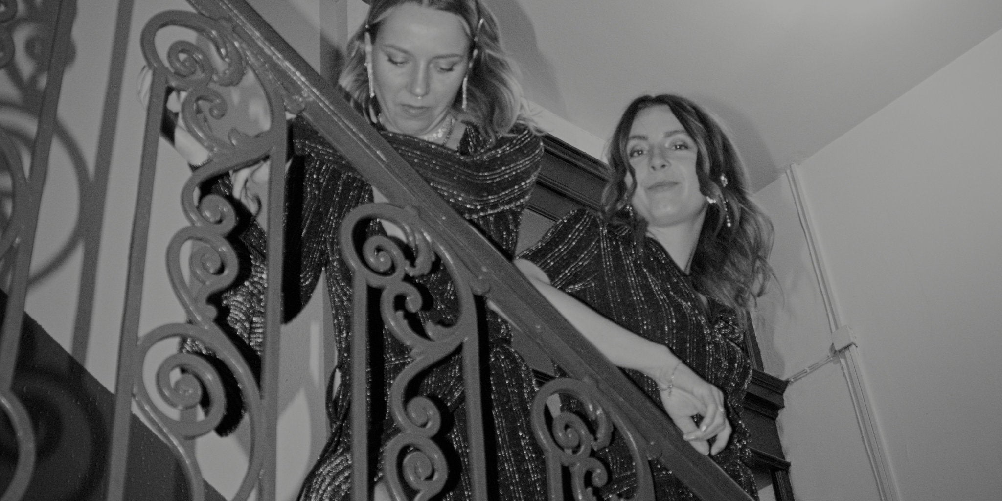 Zwei Frauen in funkelnden Abendkleidern auf einer Treppe – festliche Secondhand-Looks aus Bonnie’s Party Shop