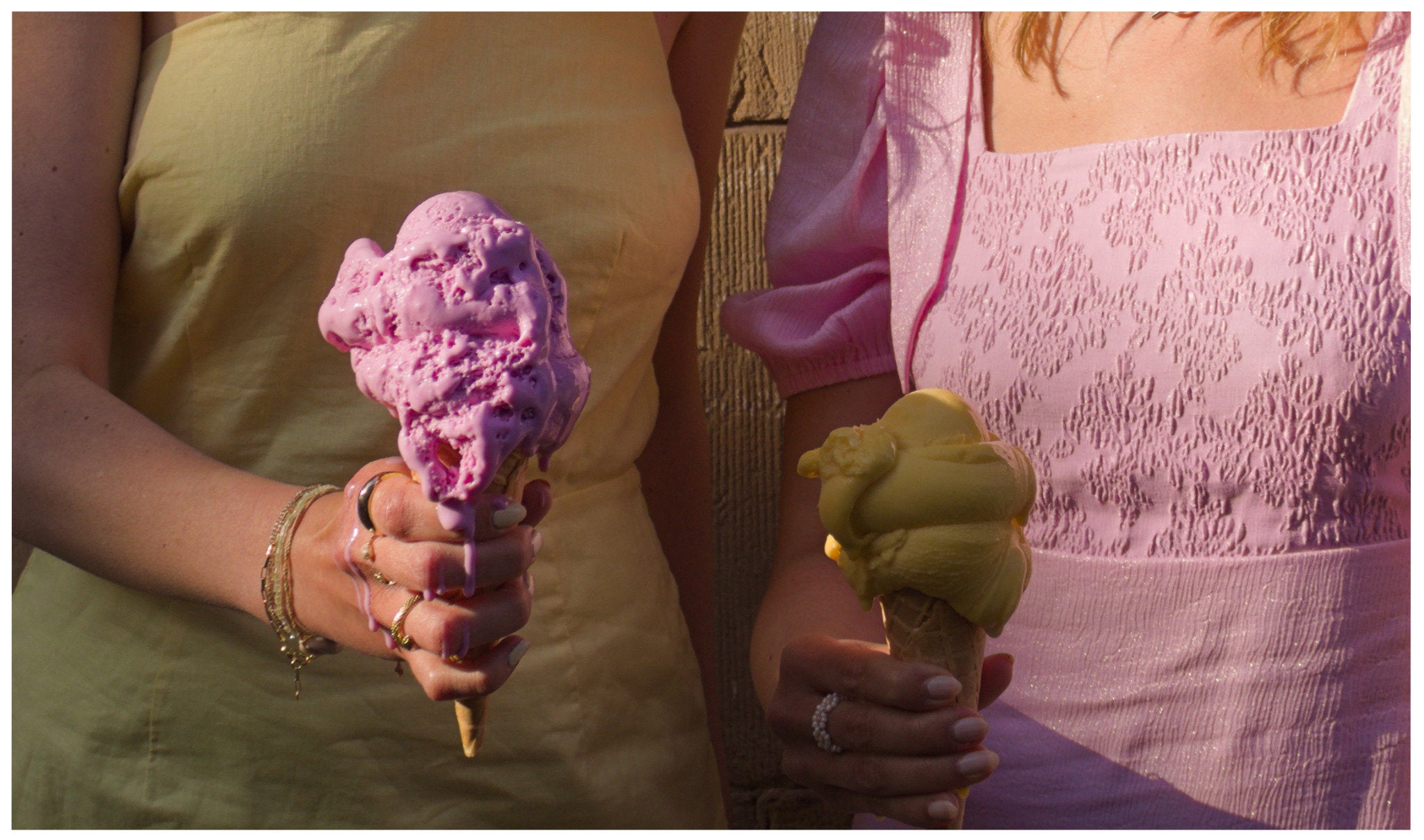 Zwei Frauen in sommerlichen Secondhand-Outfits in Pastellfarben halten schmelzendes Eis in der Hand – eine in einem gelben Leinenkleid mit pinkem Eis, die andere in einem rosafarbenen Vintage-Kleid mit gelbem Eis.
